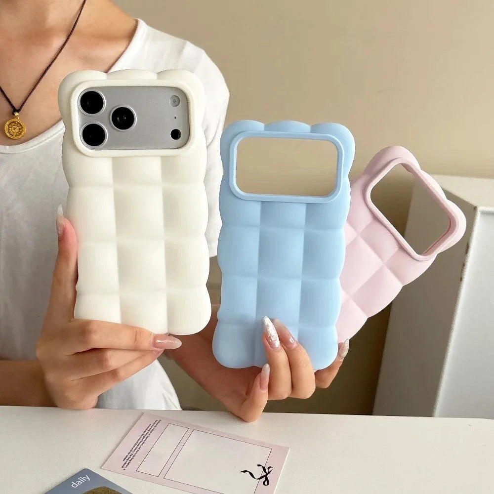 Three quilted phone cases in white, light blue, and light pink are held by a person in a white top, shown against an indoor background.